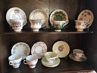 Wide view of all 8 tea cup and saucer sets displayed on shelving, showing various floral and ornate designs.