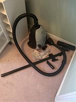 White and black Shark Plus canister vacuum with hose and various attachments including floor brush and smaller nozzles laid out on carpet.