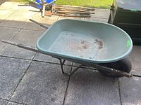 Side view of the Ames Easy Roller wheelbarrow showing weathered wooden handles, metal frame and rubber tire with tread.