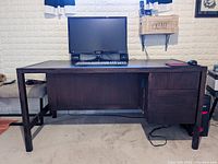 Front view of the dark wood banker desk with computer monitor and keyboard placed on top. Shows the size, cupboard door, and drawer section of the desk.