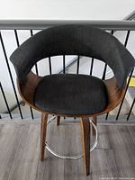 Front view of dark grey fabric swivel bar stool showing curved backrest with wood panel and wooden legs with metal footrest.