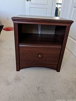 Wood veneer bedside table with a drawer and open shelf, showing dark brown finish and beveled edges.