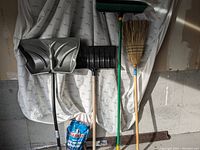 Photo showing two snow shovels, two brooms, and a bag of Alaskan ice melt standing upright against a white backdrop.