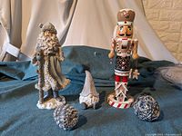 Photo of 14-inch nutcracker, 13-inch Santa figurine, small gnome figurine, and three small silver ornaments on fabric background.
