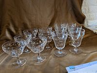 Photo showing a set of 14 clear glass stemware pieces including 8 taller wine glasses and 6 shorter dessert glasses with etched floral patterns, arranged on a cloth background.