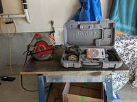 Photo shows the Black & Decker circular saw on a wooden table next to an open grey plastic carrying case containing the Dremel Saw-Max tool and multiple blades.