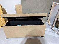 Photo of beige upholstered storage bench with lid open showing interior storage space.
