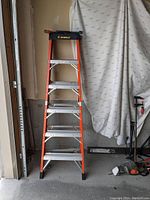6-foot fiberglass ladder orange with silver metal steps, black feet, standing upright indoors.
