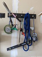 Photo of various hanging garden and watering tools including hedge trimmer, sprinkler, blue garden hose, caulking tool, Husky spirit level, and LED work light