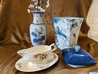 Photo of four blue and white themed household items on brown background: decorative vase, planter, blue canister with lid, and floral gravy boat on plate.
