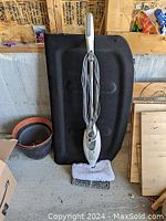 Shark steam mop shown upright against a black board with cord wrapped around handle and microfiber mop attached. Includes base accessory for rug steaming.