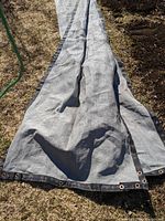 Full length view of the gray privacy tarp with metal grommet rings laid out on grass and soil surface.