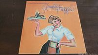 Front cover of the American Graffiti soundtrack vinyl LP featuring illustrated retro waitress artwork with diner food on tray.