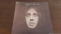 Front cover of Billy Joel 'Piano Man' vinyl album showing a surreal, sculpted face with monochrome colors.