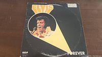 Front cover of the Elvis Presley Forever vinyl album featuring a photo of Elvis Presley singing and orange/white design graphics.