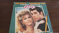 Front cover of Grease soundtrack album showing John Travolta and Olivia Newton-John with the title and movie credit text.