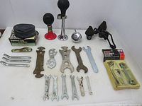 Photo showing assortment of brushes, inner tube box, repair wrenches, air horns, metal bicycle seat with springs and retro bell arranged on white surface.