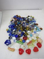 Overall view of mixed glass pebbles and marbles in various colors including blue, brown, yellow, and clear on a white surface