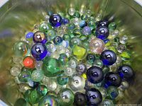 Photo of assorted glass marbles showing different colors and sizes, including large dark blue, green, and clear marbles.