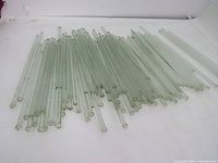Lot of multiple greenish glass rods laid out on surface, showing quantity and appearance