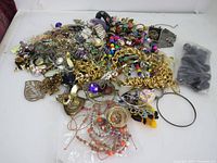 Pile of assorted mixed broken jewelry including metal chains, beads, and various costume jewelry pieces in different colors and styles
