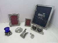 Photo showing 8 pewter items including 4 picture frames, sun catcher, candle holder, note clip, angel ornament arranged on white surface.