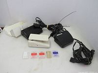 Lot of three sewing machine foot pedals and five packs of new sewing needles arranged on white background. Two Kenmore pedals (one black one white), one black Singer pedal. New needles in various colored packages visible.