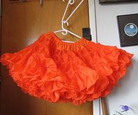 Orange square dance skirt hanging against a wooden door, showing the full silhouette and ruffled layers.
