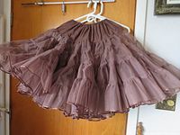 Brown square dance skirt hanging on white plastic hanger showing gathered elastic waistband and full ruffled single-layered fabric.