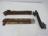 Top view of two sliding barn gate latches and one door spring showing rust and metal surface condition.