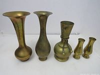 Five vintage brass vases of varying shapes and sizes shown against a plain background, exhibiting used patina and minor tarnish.