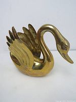 Front side view of the brass swan figurine with detailed folded wings and arched neck.