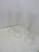Five clear vintage oil lamp chimneys grouped together on flat surface, showing size and shape