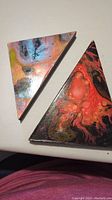 Two triangular abstract paintings each with fluid art style and vibrant colors placed on white background.