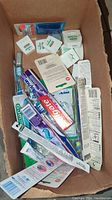 Top view of the box containing several toothbrushes and dental floss packages showing brand names and packaging condition.