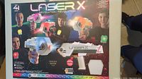 Front image of Laser X box featuring four players holding laser tag guns in red, blue, orange, and green with product info and branding.