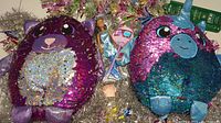 Photo showing two Shimeez plush toys with holographic sequins, a glitter boa, silver tinsel garlands, and small additional decorative figures.