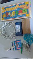 Photo showing the full lot including the extension cord, board game box, blue hand massager, two prize packages, a cardboard box, and small miscellaneous items on a white surface.