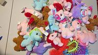 Pile of small pastel-colored plush stuffed animals including unicorns, dogs, and horses with tags attached.
