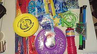 Photo showing yellow PLA frisbee, purple frisbee with star holes, bubble makers, skipping rope, and marbles.