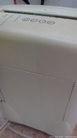 Side view of off-white plastic paper shredder unit showing overall condition and design with wheels visible at base.