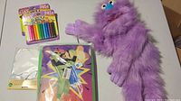 Purple furry puppet, multi-color clay set, and canvas boards on table