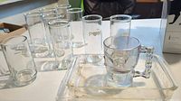 Photo showing a collection of 9 shot glasses including one with POM logo, a skull-shaped glass mug, and a rectangular glass tray
