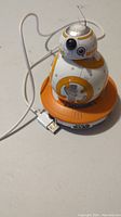 Sphero BB-8 robot toy sitting on orange charging base with USB cable plugged in.