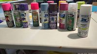 Photo of ten spray paint cans of different colors and brands lined up on table, showing varied colors and types.