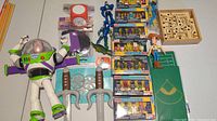View of large Buzz Lightyear, small Woody, six packages of knock off Lego figures, toy swords, wooden maze game, dinosaur toy