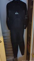 Full view of black XLS Quicksilver wetsuit hanging, showing overall design and condition.