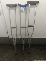 Front view of three aluminum crutches with different colored padded tops and grips, standing against a wall.
