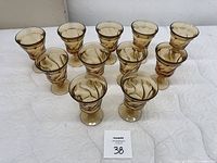 11 used amber glass goblets arranged in a group on a white textured surface, showing their full shapes and swirl glass patterns.