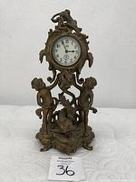 Full view of antique brass clock showing two cherub figures holding a decorative element with fish on the base.
